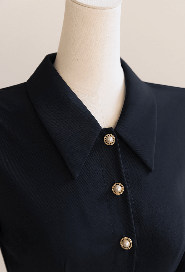 Close-up of an elegant navy dress with a structured collar and pearl buttons, showcasing refined style and detail.