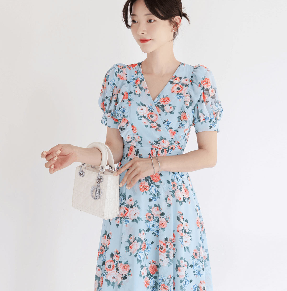 Woman wearing a blue floral chiffon dress with short puff sleeves and V-neckline, holding a white handbag, perfect for spring fashion.