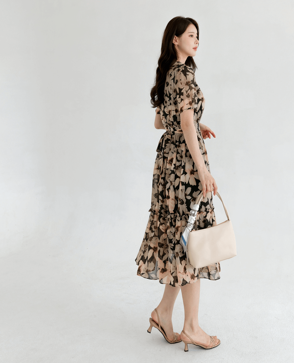 Woman wearing a floral chiffon dress with wide collar and puff sleeves, paired with beige heels and handbag.