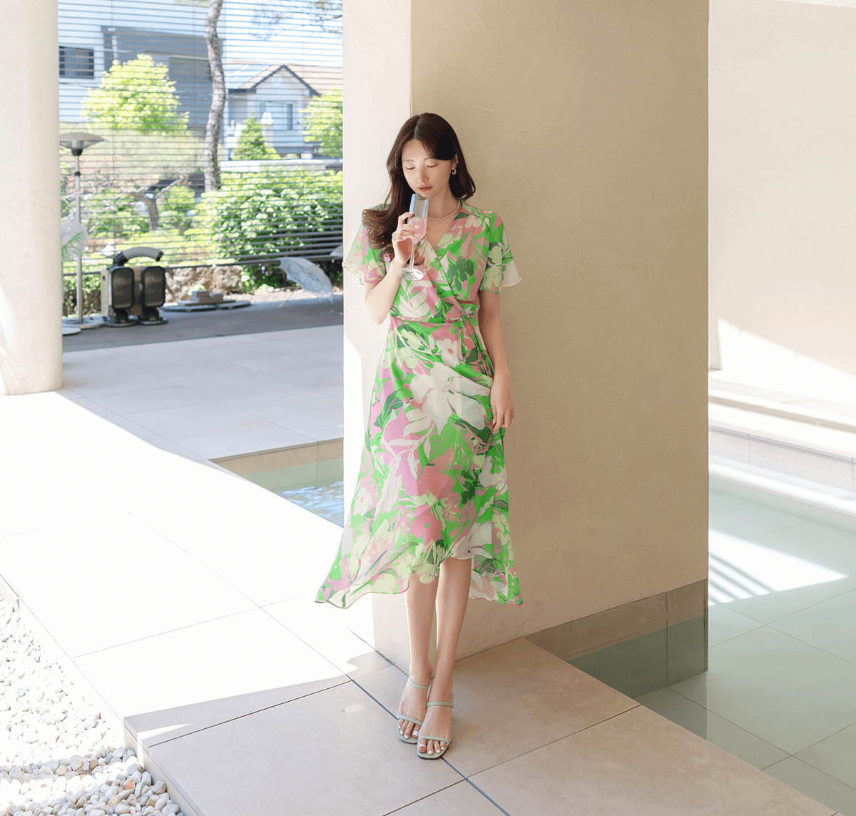 Woman in green floral chiffon wrap dress with tulip hem, enjoying a sunny day outdoors.