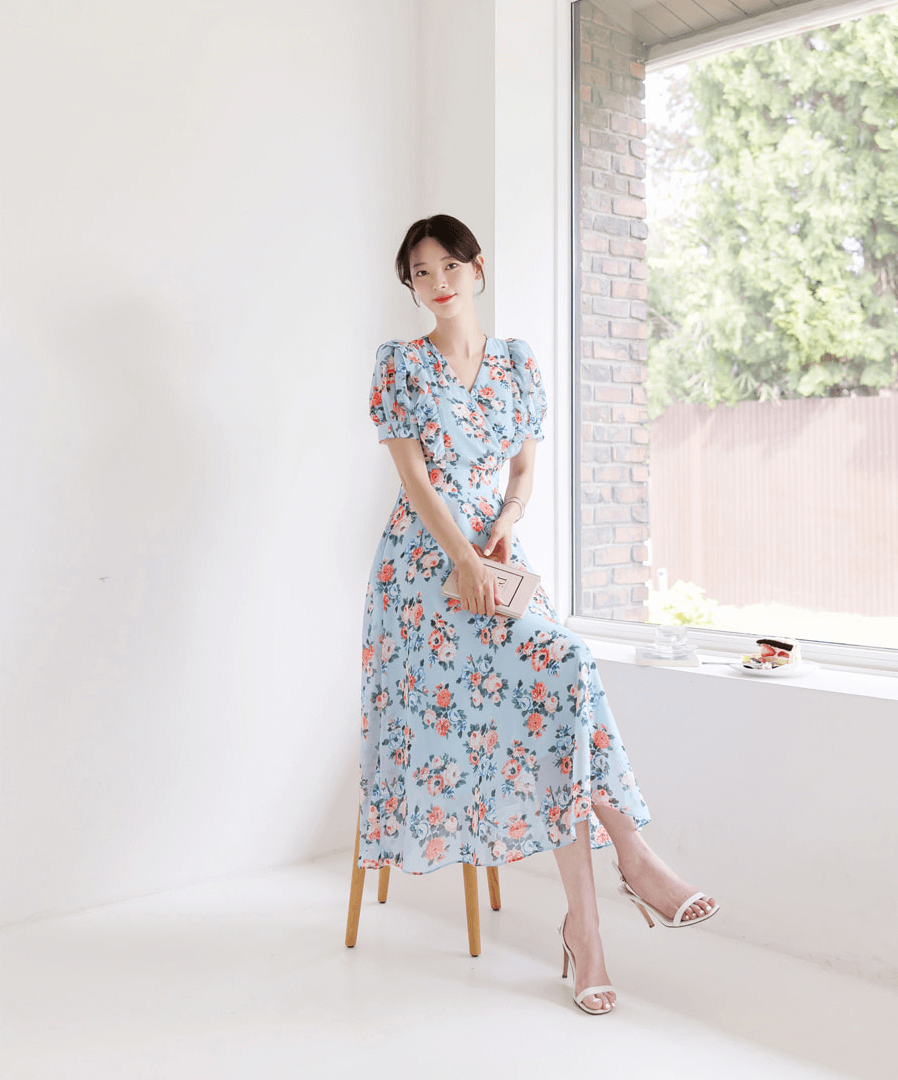Model wearing a blue romantic floral chiffon dress with short puff sleeves and V-neckline, sitting in a sunlit room.