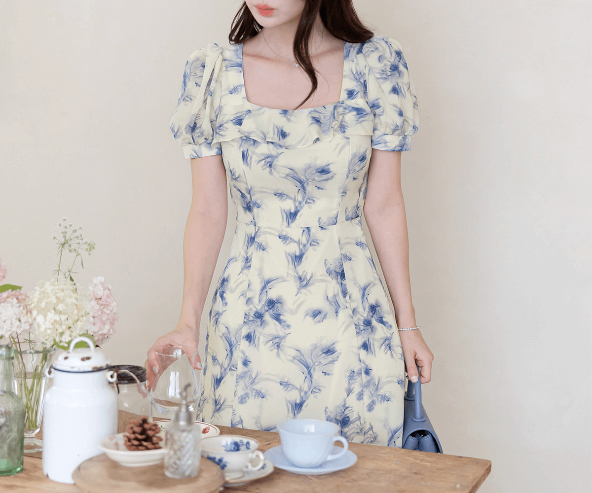 Elegant chiffon dress with blue-violet abstract print and ruffled square neckline, surrounded by a serene table setting.