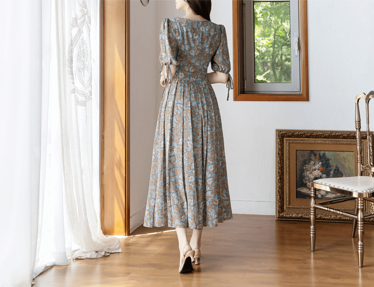 Woman in pleated dress with shoulder-to-hem slit sleeves and ribbon ties, featuring a square neckline and A-line silhouette.