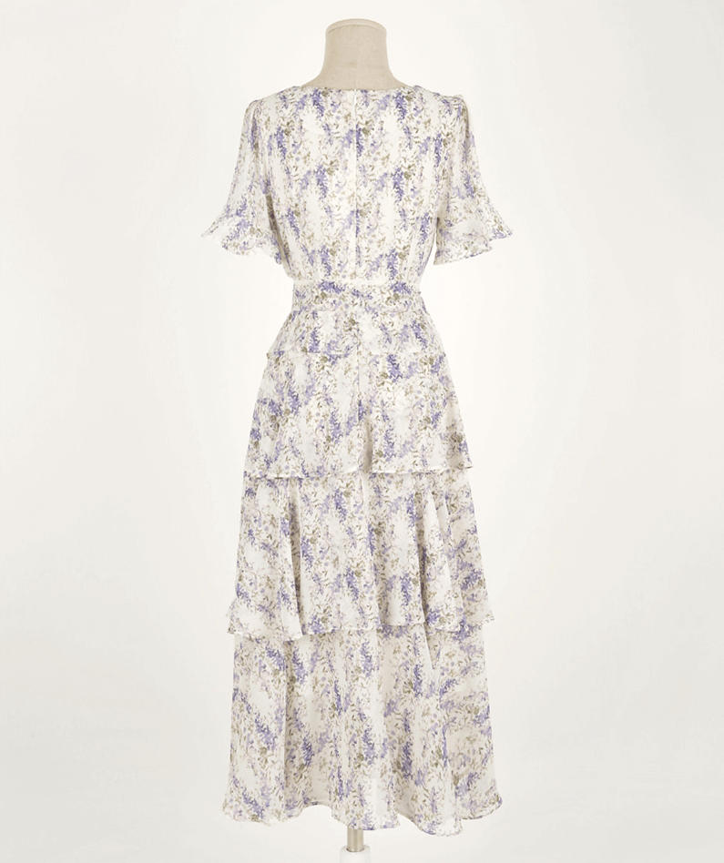 Back view of an asymmetrical tiered floral chiffon dress with purple blossoms on a beige base, featuring a feminine silhouette.