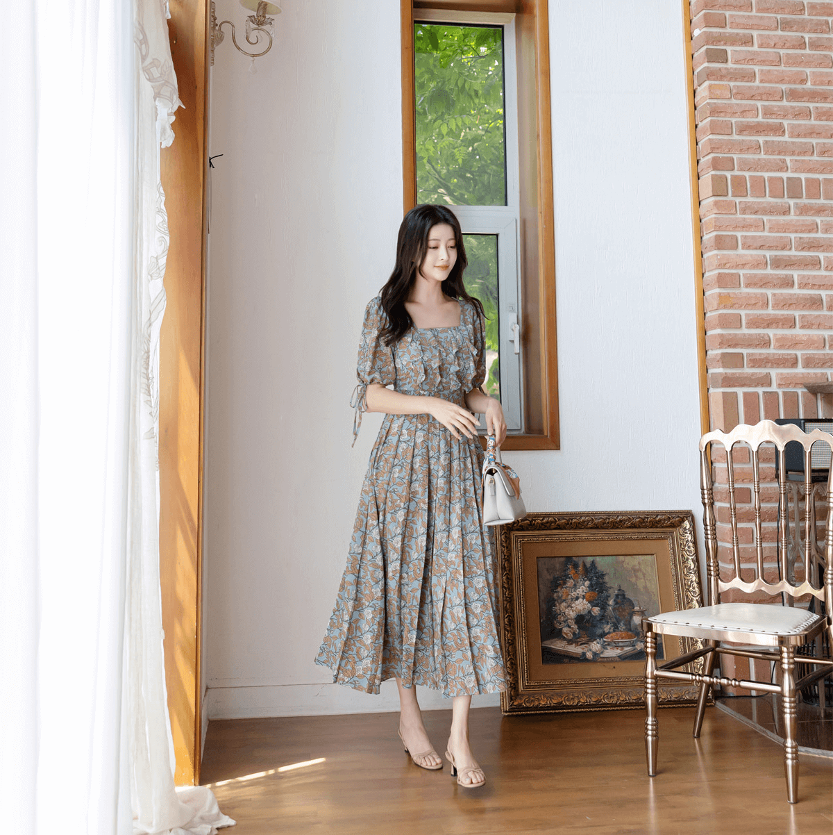 Woman wearing pleated dress with shoulder-to-hem slit sleeves and ribbon ties, standing indoors by a window.