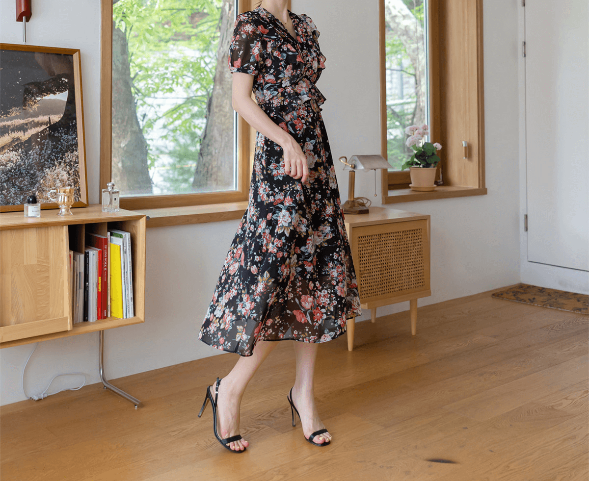 Woman wearing a floral chiffon dress with pintuck bodice and peplum, featuring black base color, V-neckline, and puffed sleeves.