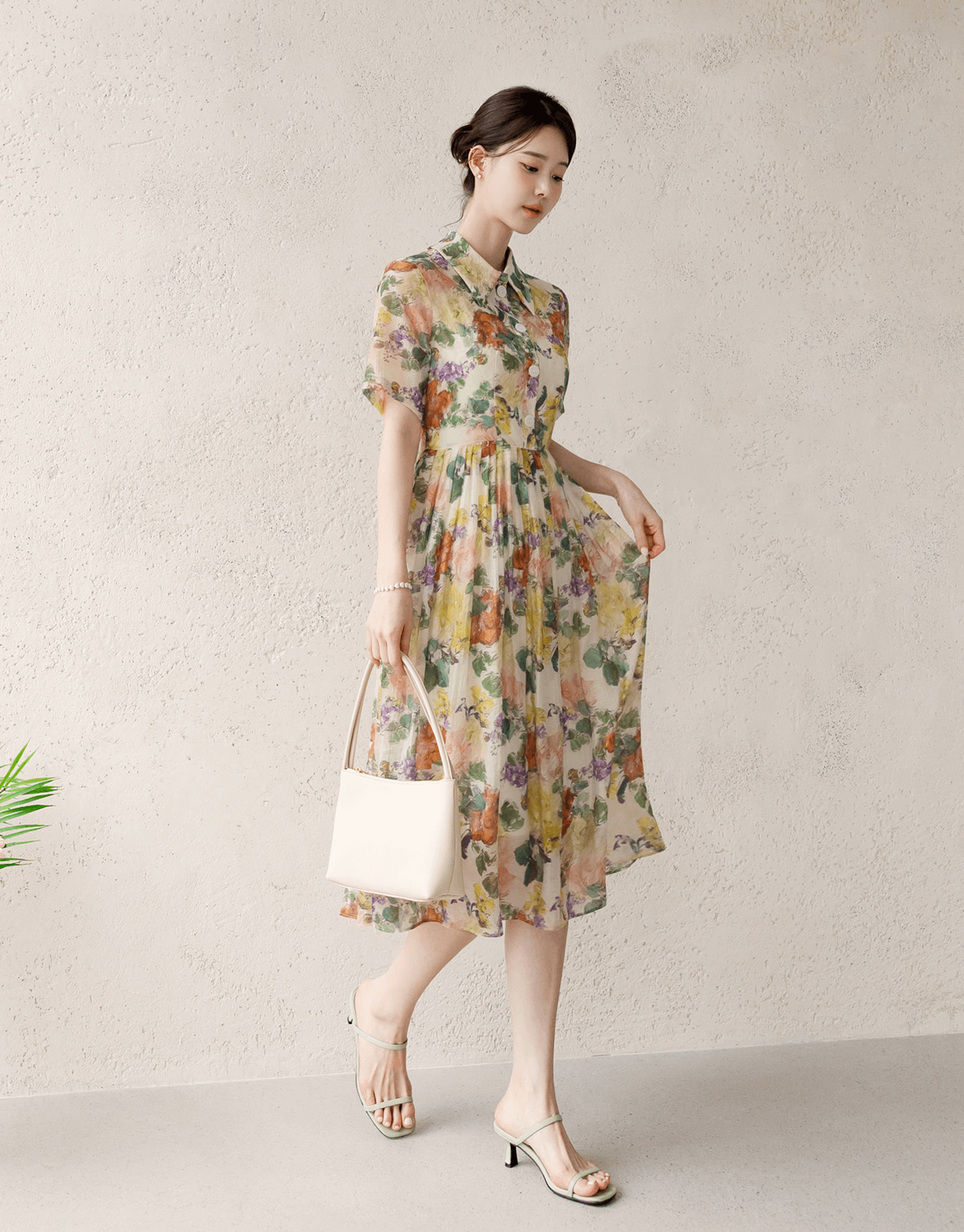 Woman wearing a romantic floral dress with pintuck detailing and collar neckline, soft flare silhouette, holding a white handbag.