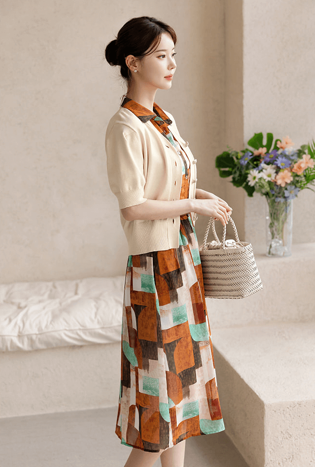 Woman wearing a patterned shirt dress with soft cap sleeves, classic collar, and faux leather belt, holding a woven handbag.