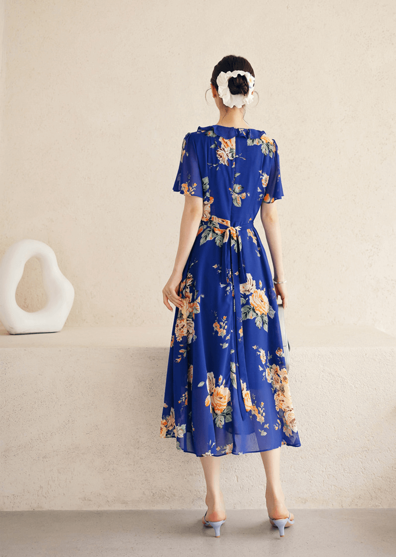 Back view of a floral chiffon dress in blue with sheer wing sleeves and square neckline, styled on a mannequin against a neutral background.