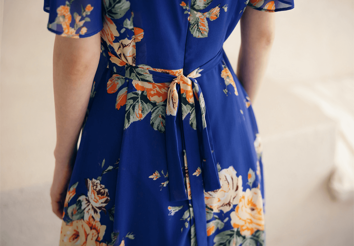 Back view of blue floral chiffon dress with sheer wing sleeves and tie waist, showcasing detailed flower pattern.