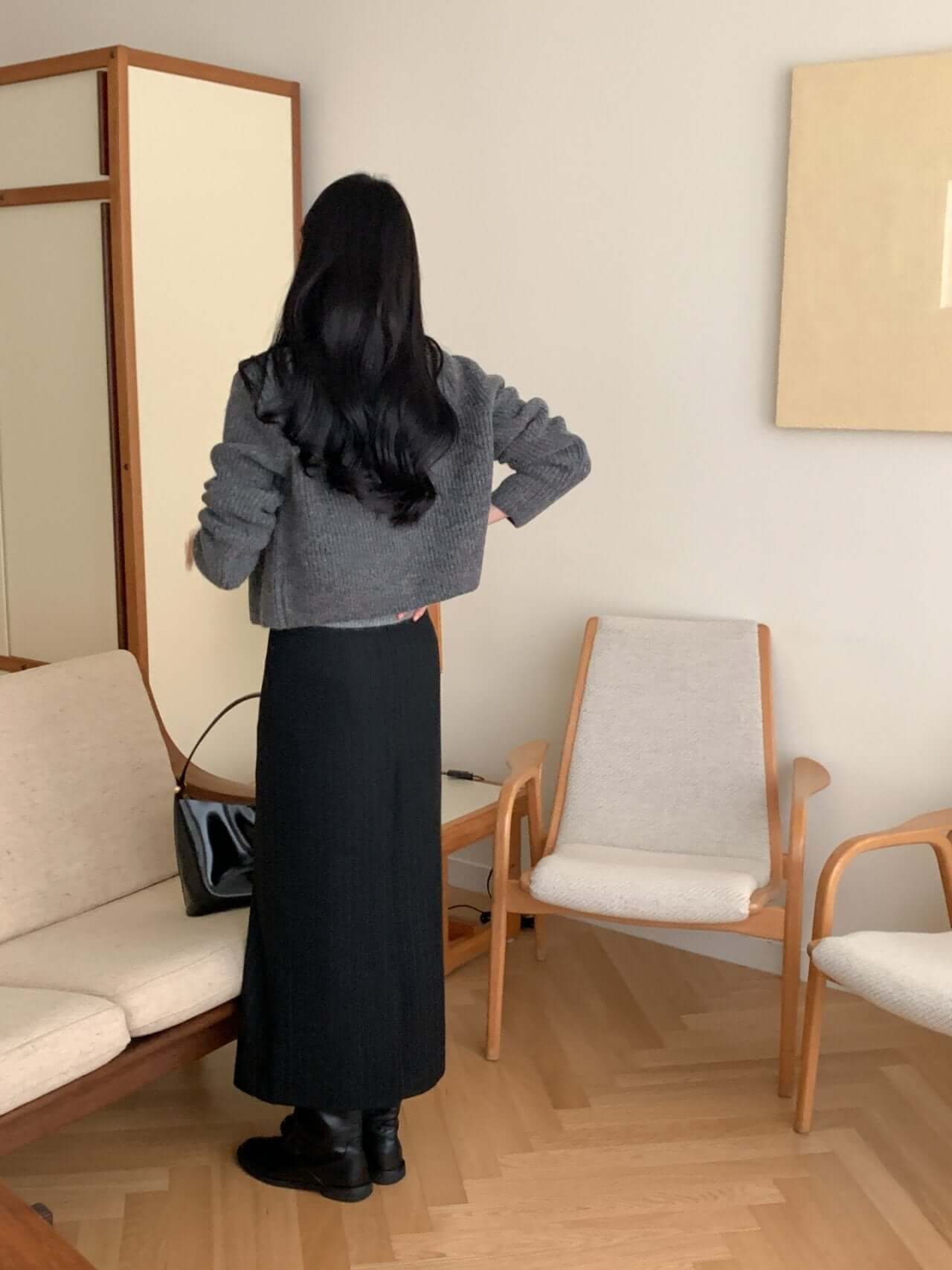 Woman wearing a gray alpaca blend cardigan with a black skirt, seated in a stylish, modern living room.