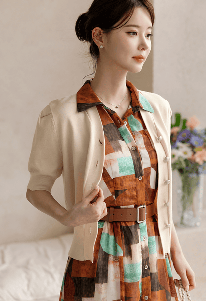 Woman in patterned shirt dress with soft cap sleeves, classic collar, and faux leather belt, styled with cream cardigan.