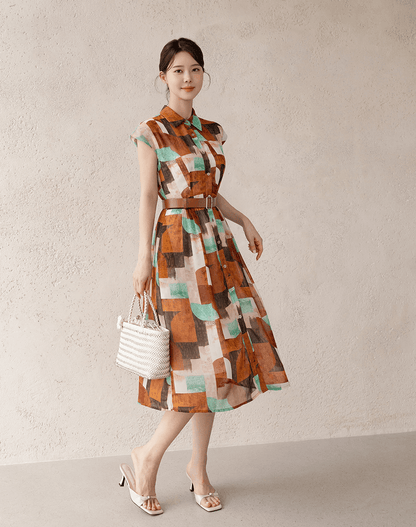 Woman in patterned shirt dress with cap sleeves and belt, holding a white handbag.