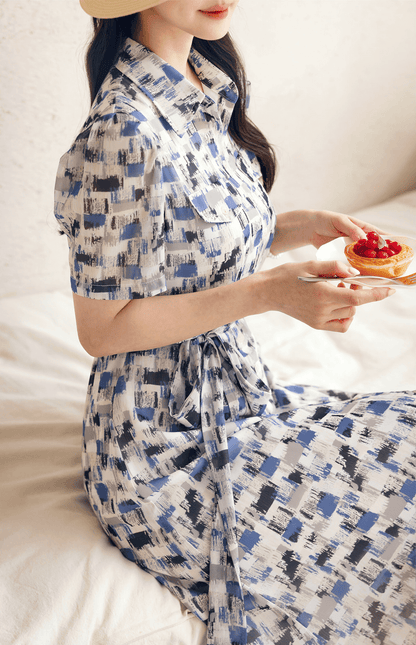 Woman in a blue abstract-patterned chiffon shirt dress with belt, enjoying dessert on a sunny day.