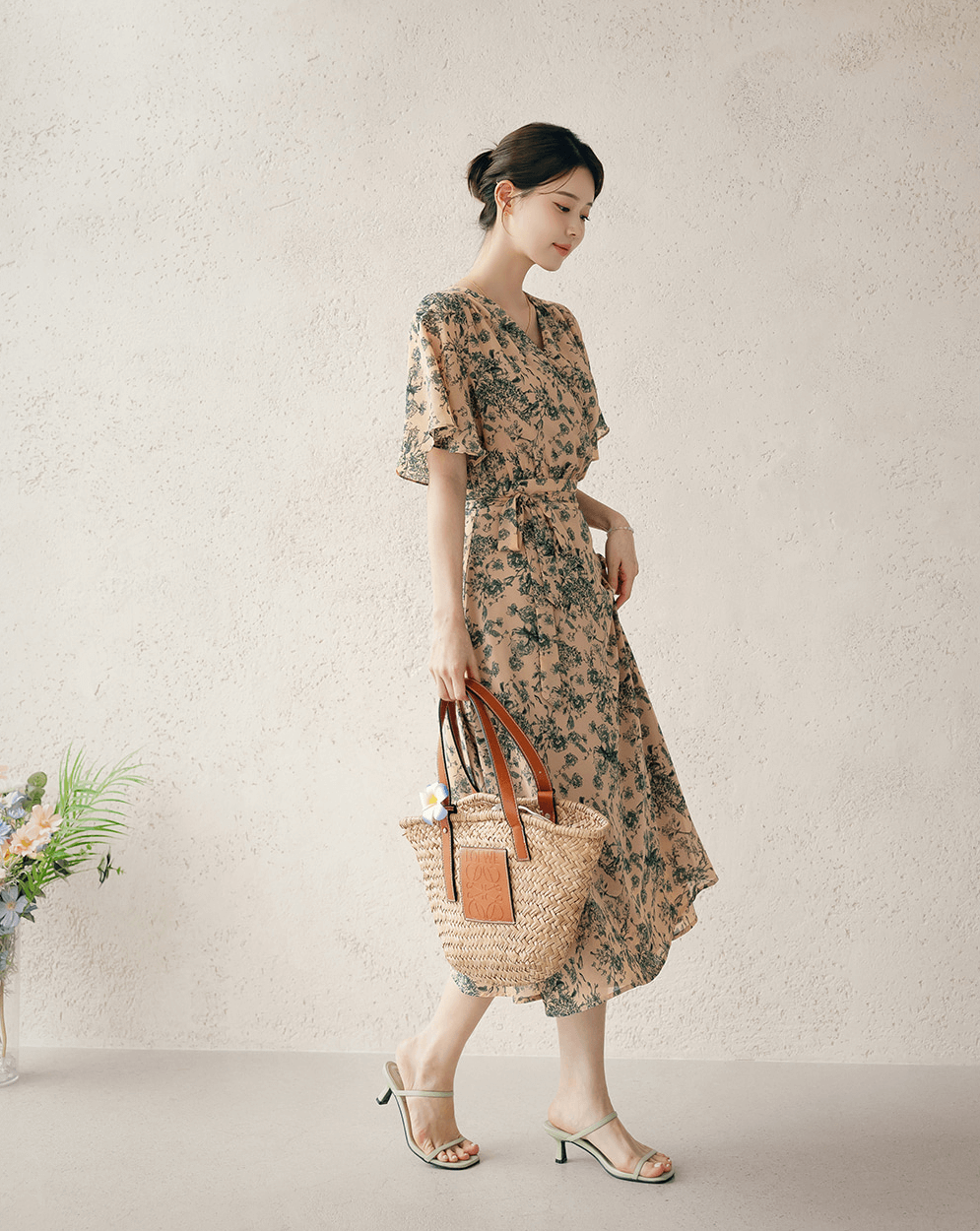 Model wearing goddess-inspired wrap dress with wing sleeves and holding straw handbag, showcasing elegant and feminine design.