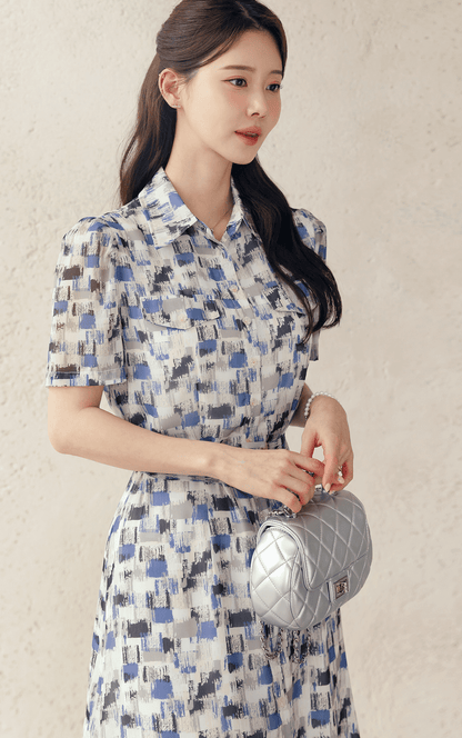 Woman wearing Breezy Chiffon Shirt Dress with blue abstract pattern and matching belt, accessorized with a white quilted handbag.