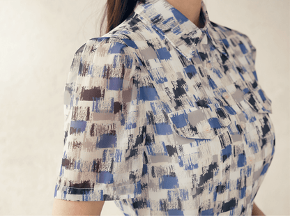 Close-up of a breezy chiffon shirt dress with an abstract blue pattern and collar neckline, highlighting short sleeves and chest pockets.
