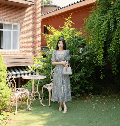 Woman wearing pleated dress with slit sleeves and ribbon ties, standing in a garden setting.