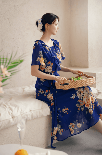 Woman wearing a floral chiffon dress with sheer wing sleeves and square neckline, sitting with a fruit basket.